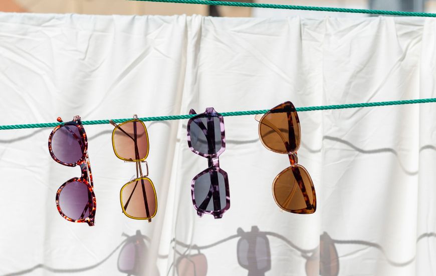 cuatro gafas de sol de distintos colores colgadas en un tendedero de ropa